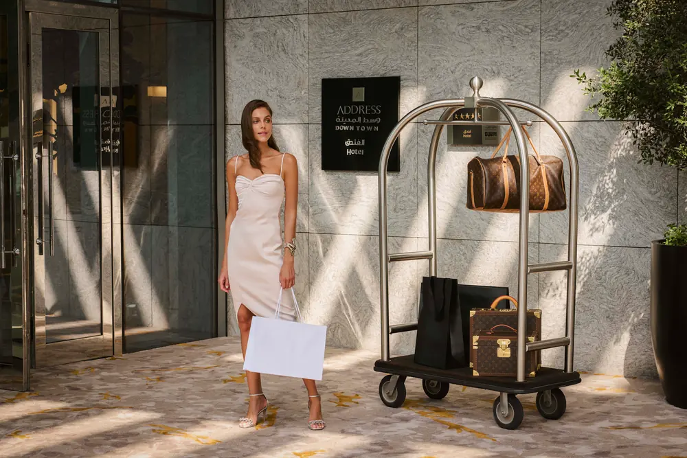 A guest at the entrance to Address Downtown beside a luggage trolley