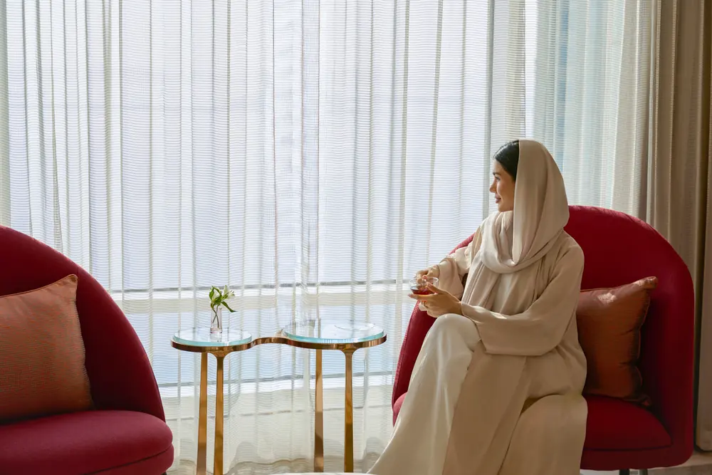 A guest taking tea in the lounge at Andaz Doha, the window screened in sheer white