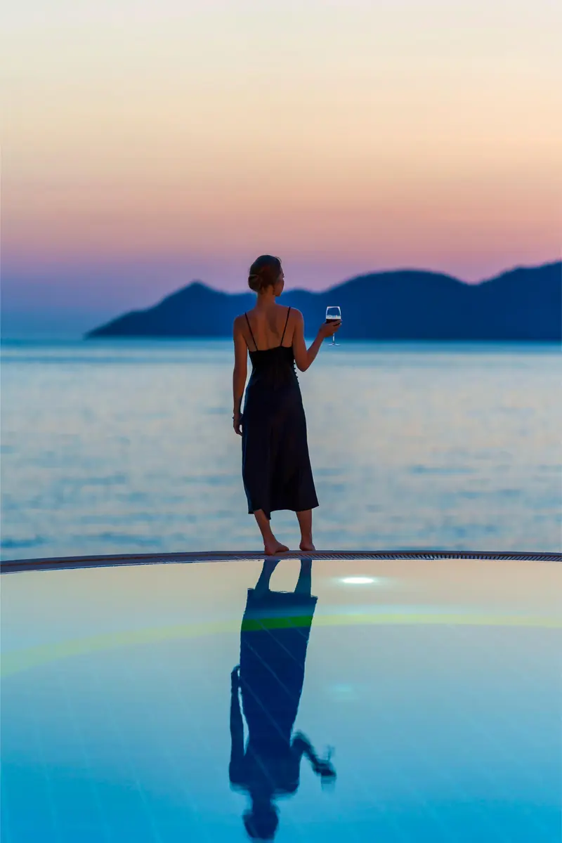 A guest at the pool edge at Liberty Lykia at dusk, the islands beyond