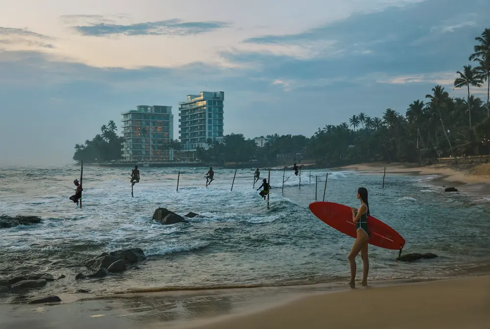 The coastline beside the resort at Galle, with stilt fishermen offshore and a surfer on the sand