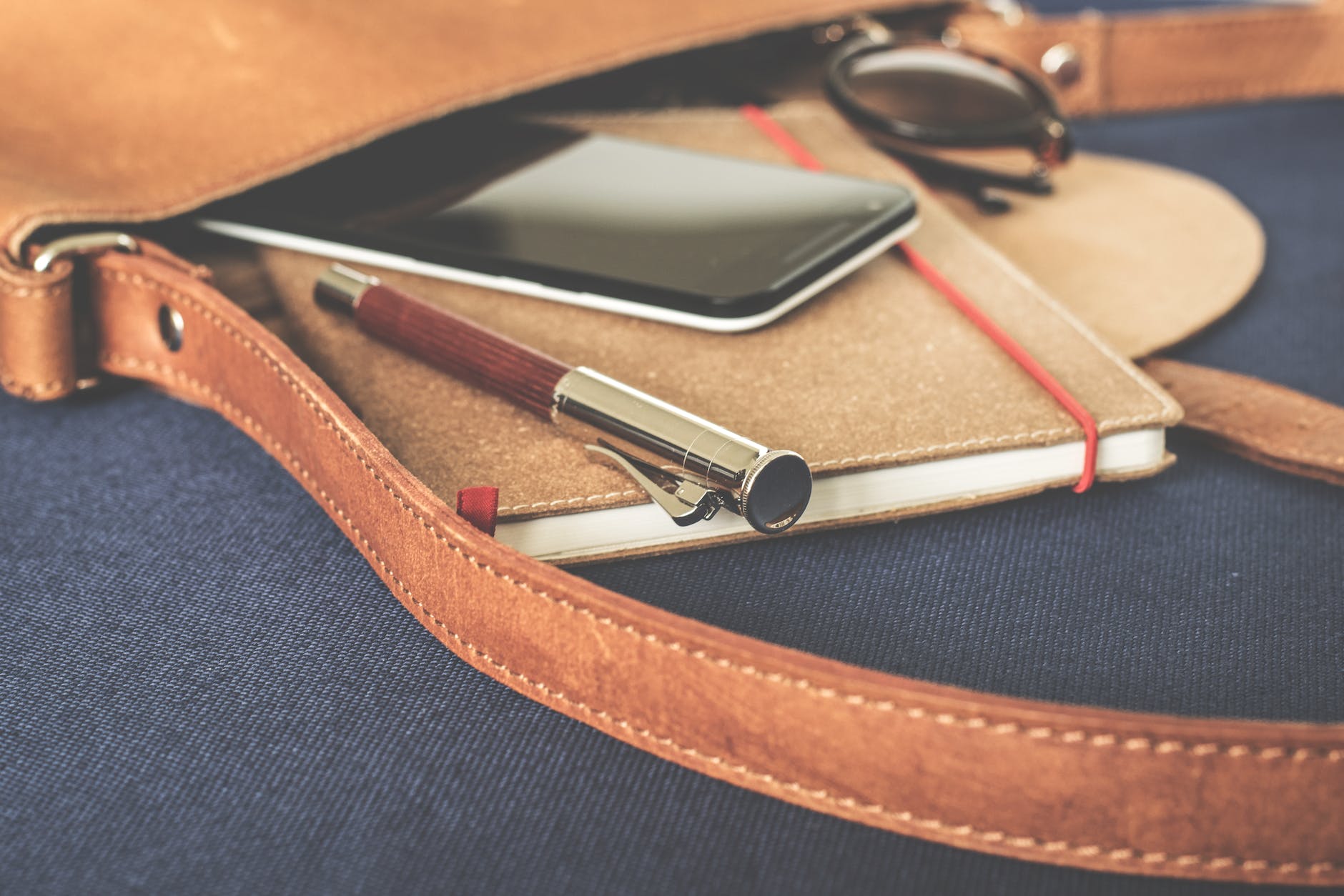 smartphone displaying black screen on notebook beside pen and sunglasses